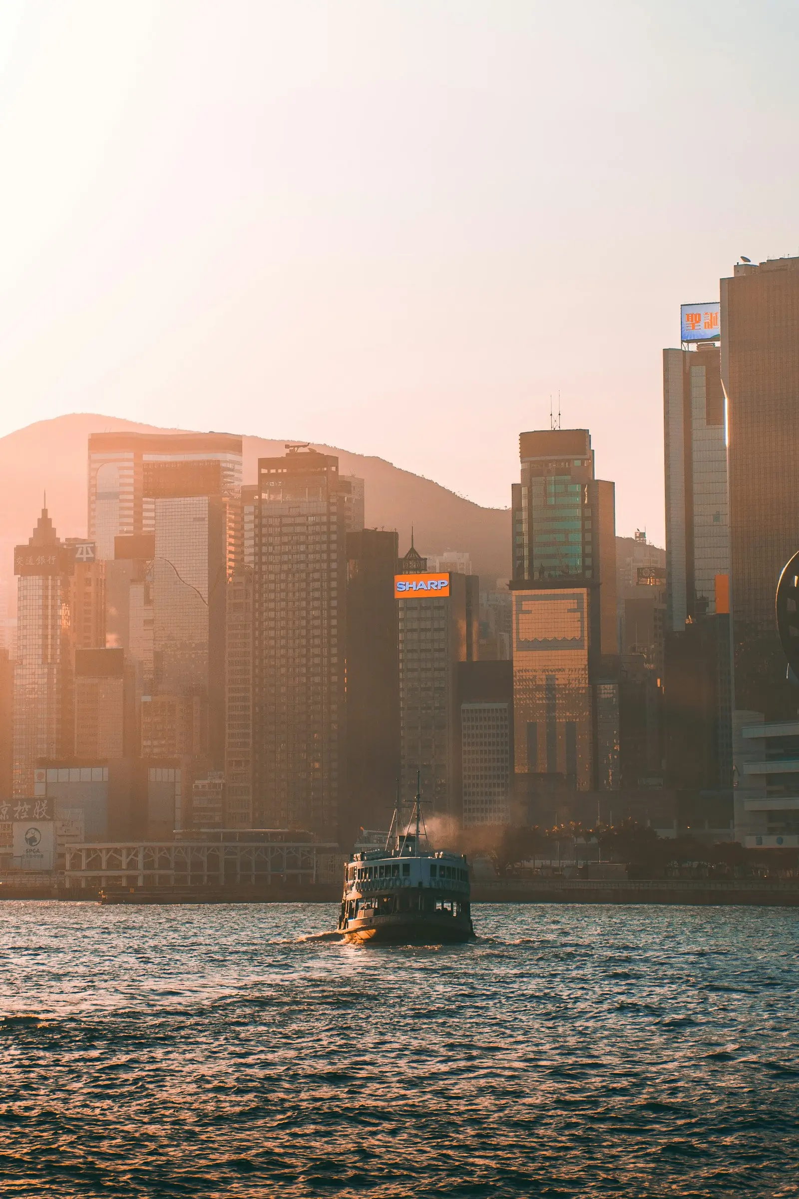Hong Kong skyline at golden hour with a boat on Victoria Harbour