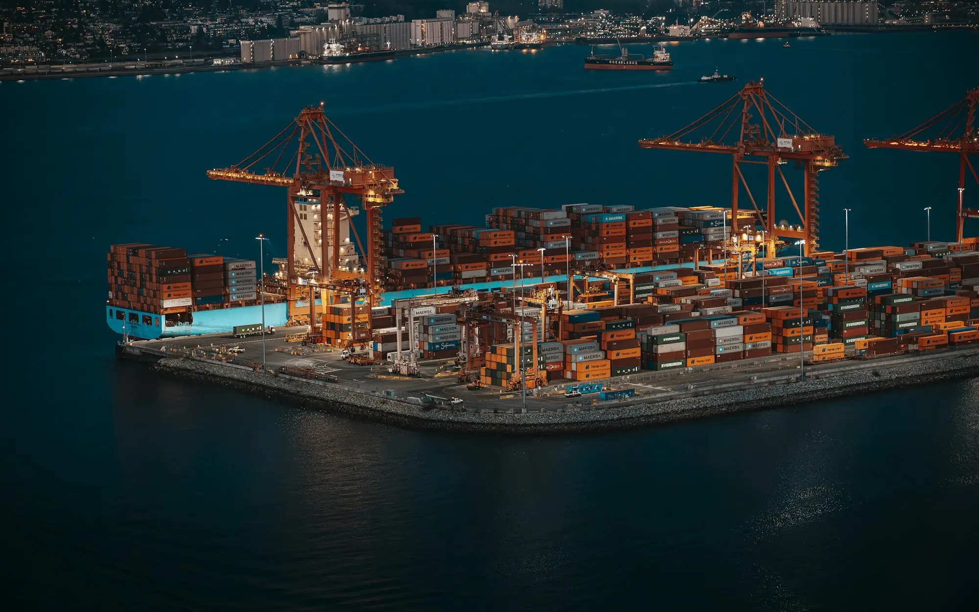 Container port at dusk with cranes and illuminated container stacks